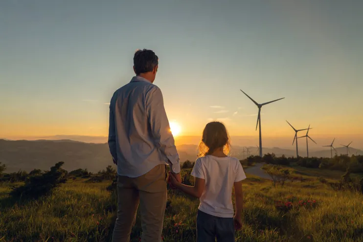 Young father and daughter looking towards a group of wind turbines at sunset