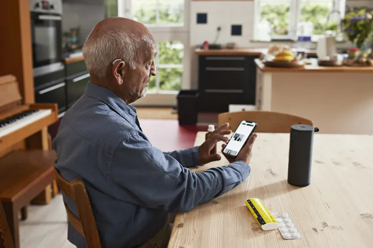 Older man with a hearing aid using a smart phone at a table