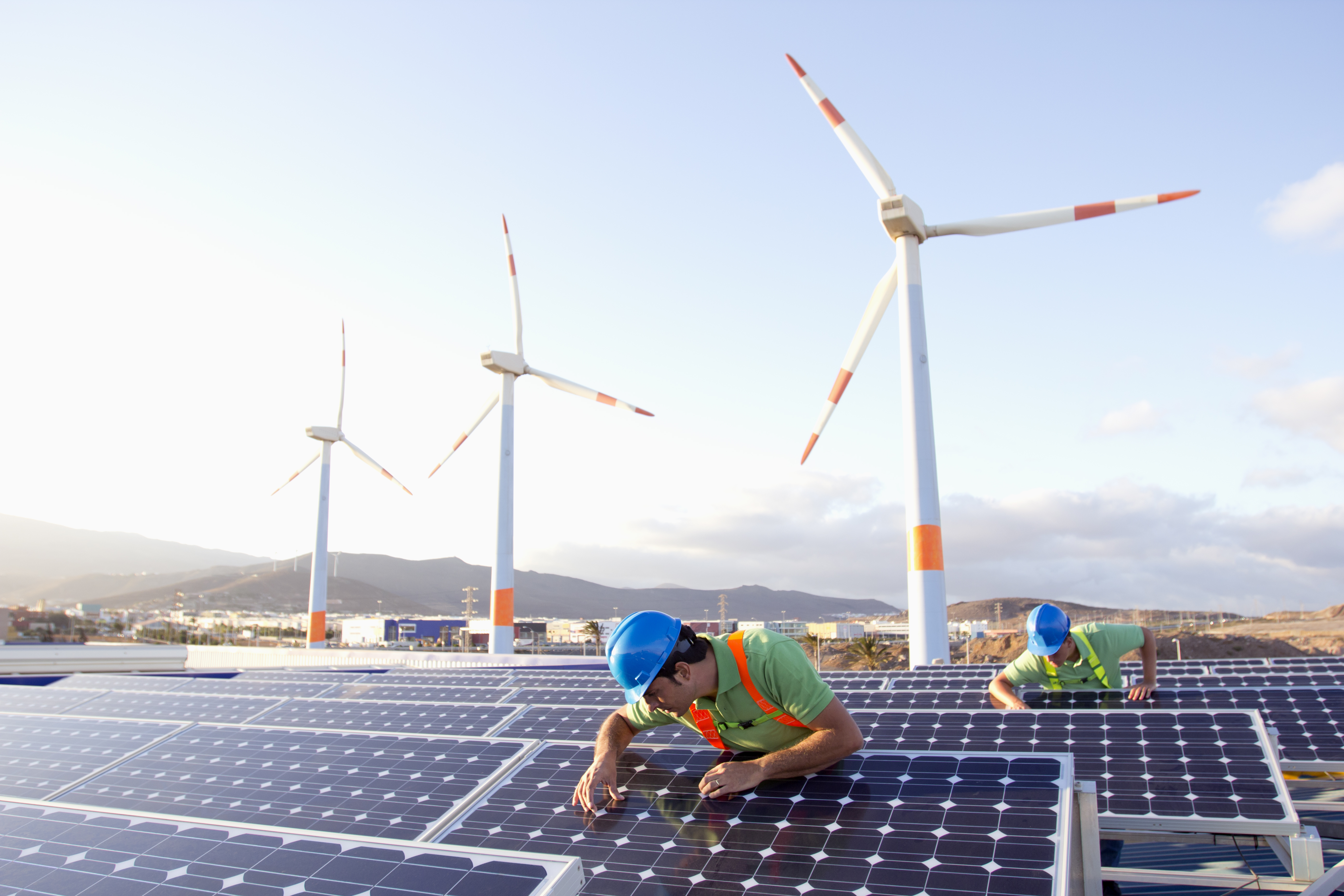 Engineers working on a solar farm next to wind turbines
