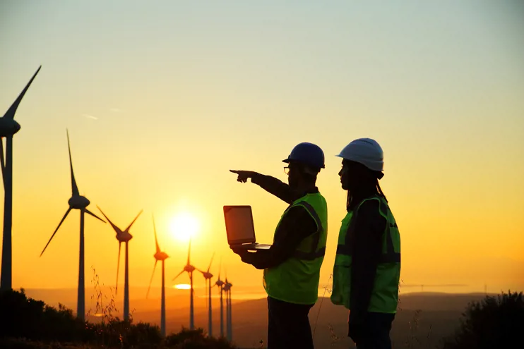 Two engineers standing in front of a row of wind turbines with the sun low on the horizon