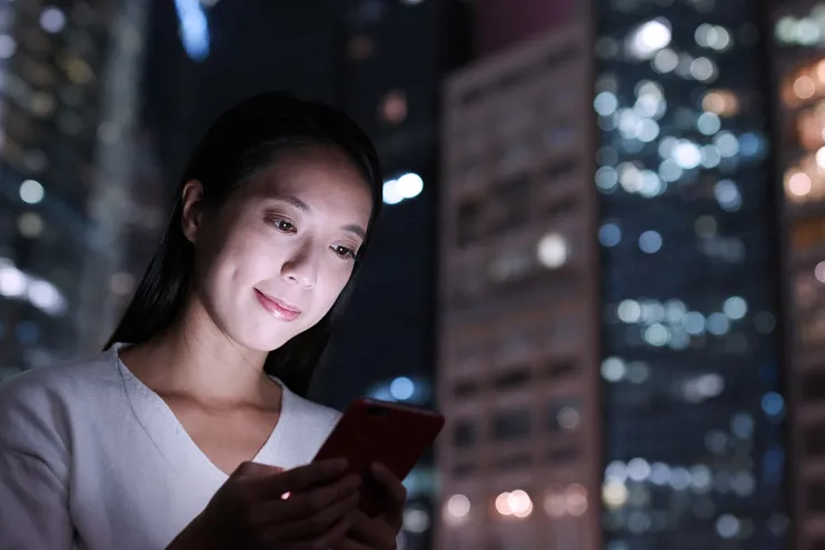 young Asian woman on mobile phone with a modern city skyline at night behind