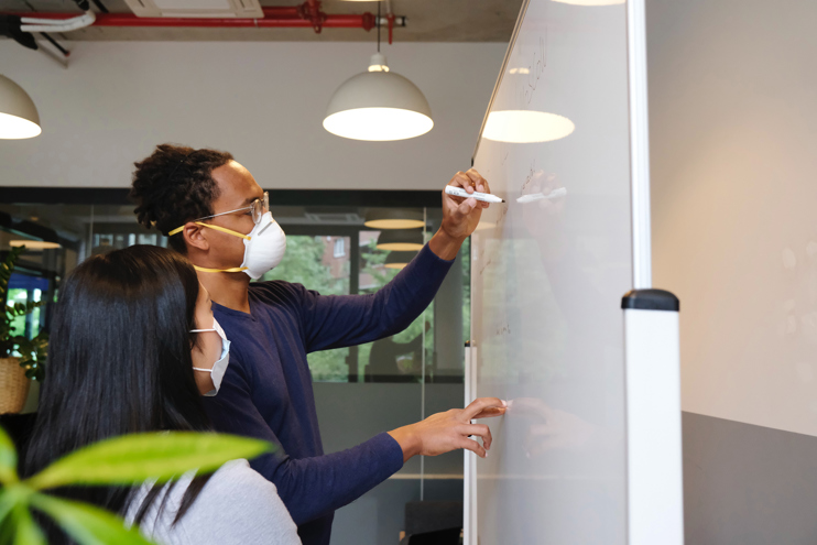 Two women in face masks in front of a whiteboard