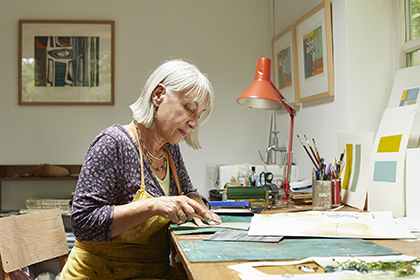 Image of a lady at a desk wearing an apron working on art